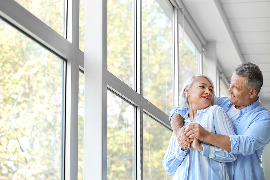 Happy senior couple embracing by large window
