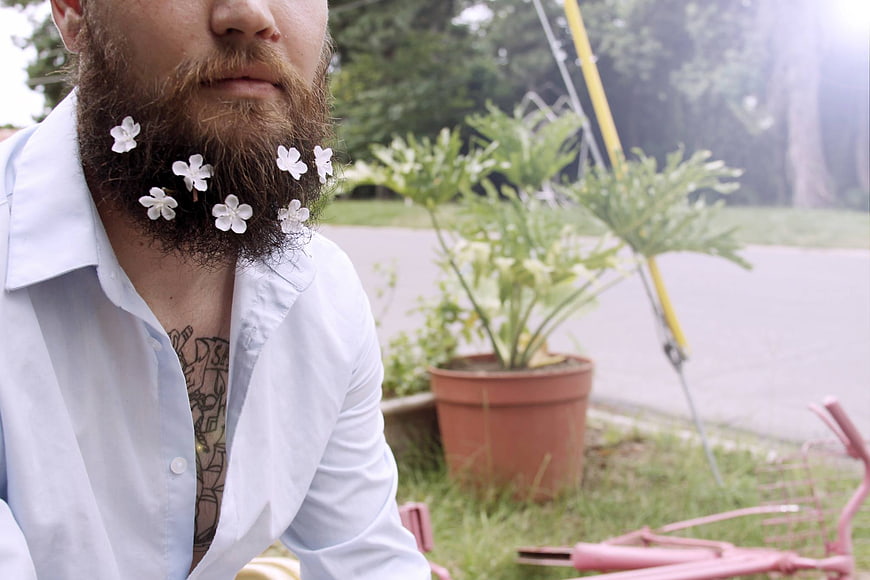 Man with white flowers in beard outdoors