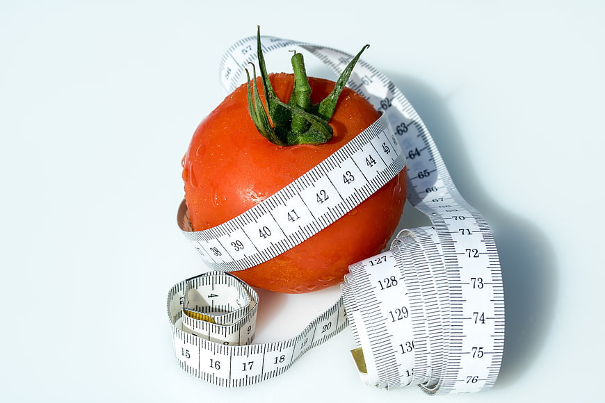 Fresh Tomato Wrapped in Measuring Tape on White Background