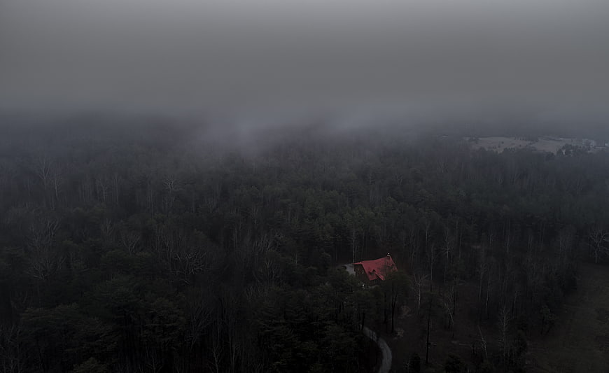 Aerial view of red-roofed cabin in foggy forest