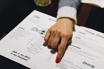 Woman pointing at restaurant menu with red nail polish
