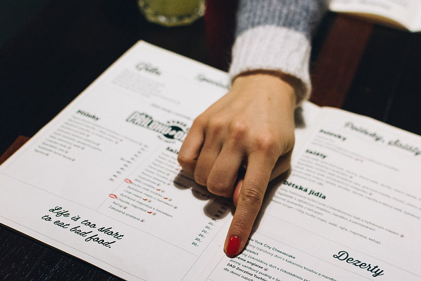 Woman pointing at restaurant menu with red nail polish