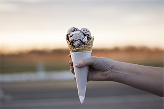 Hand holding chocolate chip ice cream cone at sunset