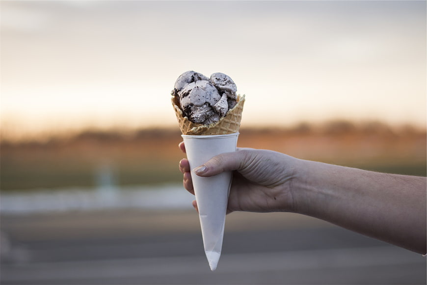 Hand holding chocolate chip ice cream cone at sunset