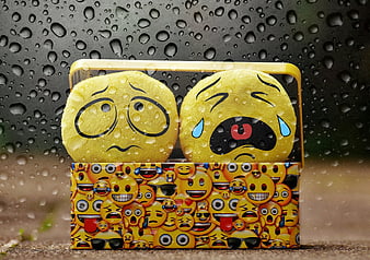 Sad emoji plush toys in rain with water drops