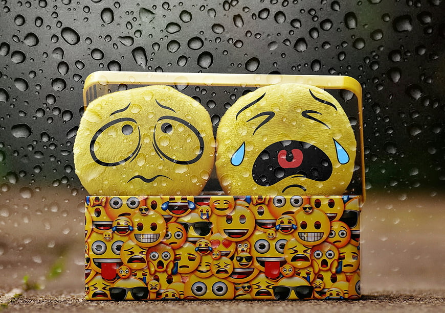 Sad emoji plush toys in rain with water drops