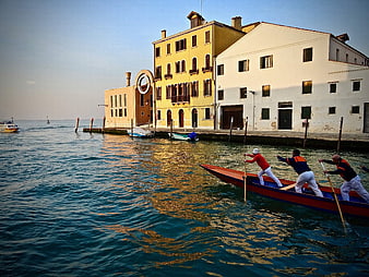 Rowers in a red boat on a Venetian canal with historic buildings
