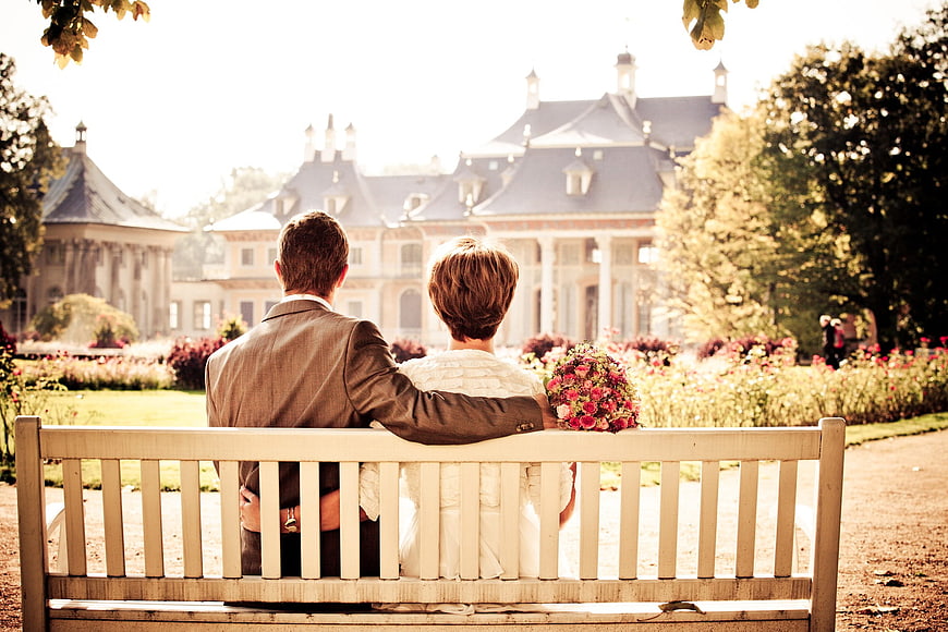 Bride and groom sitting on bench facing chateau