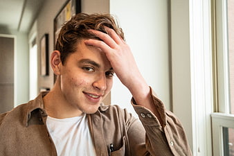 Young man smiling with hand on head in casual indoor setting
