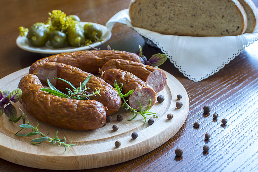 Gourmet sausages with herbs, peppercorns, and bread on wooden board