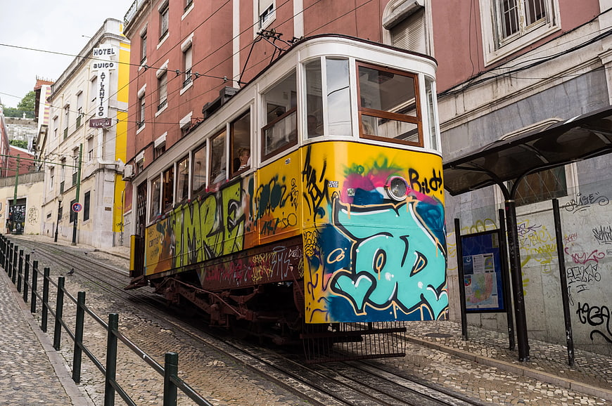 Graffiti-covered yellow tram on cobblestone street in Lisbon