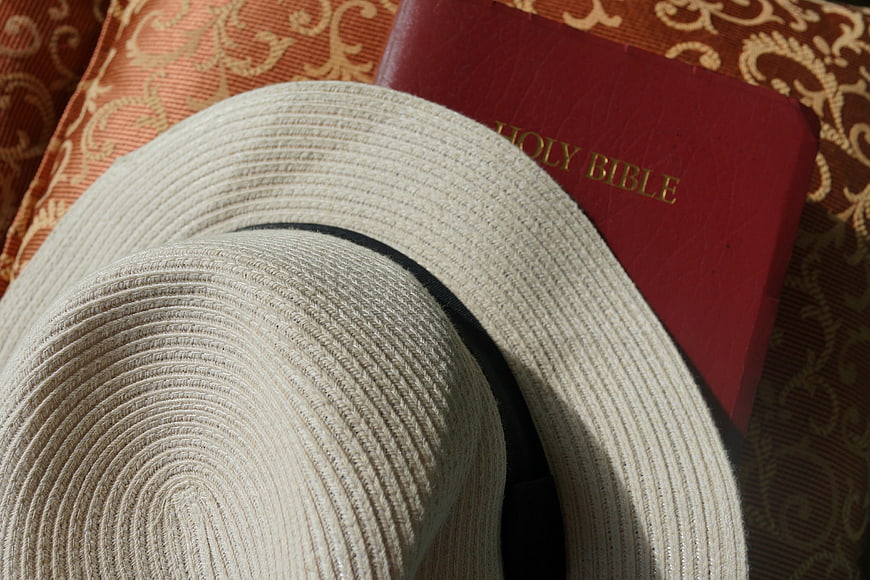Straw hat and red Holy Bible on patterned fabric