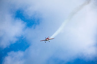 Red Aerobatic Plane Flying with Smoke Trail in Blue Sky