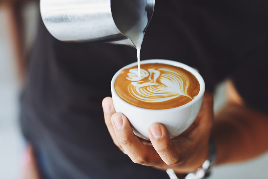 Barista pouring latte art into a white coffee cup