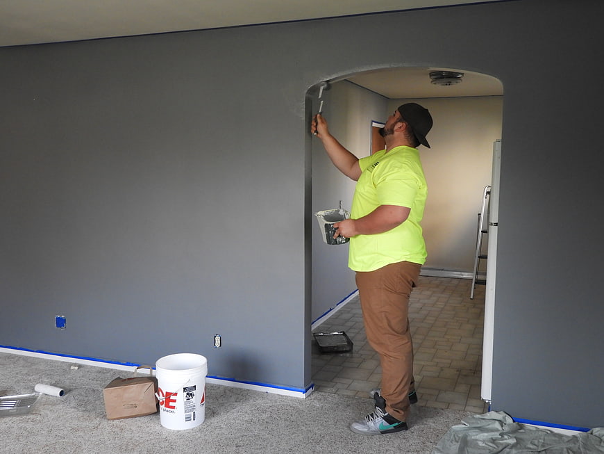 Painter applying gray paint to interior wall with roller