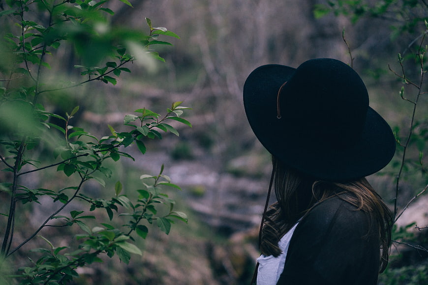 Woman in Black Hat Looking at Forest Stream