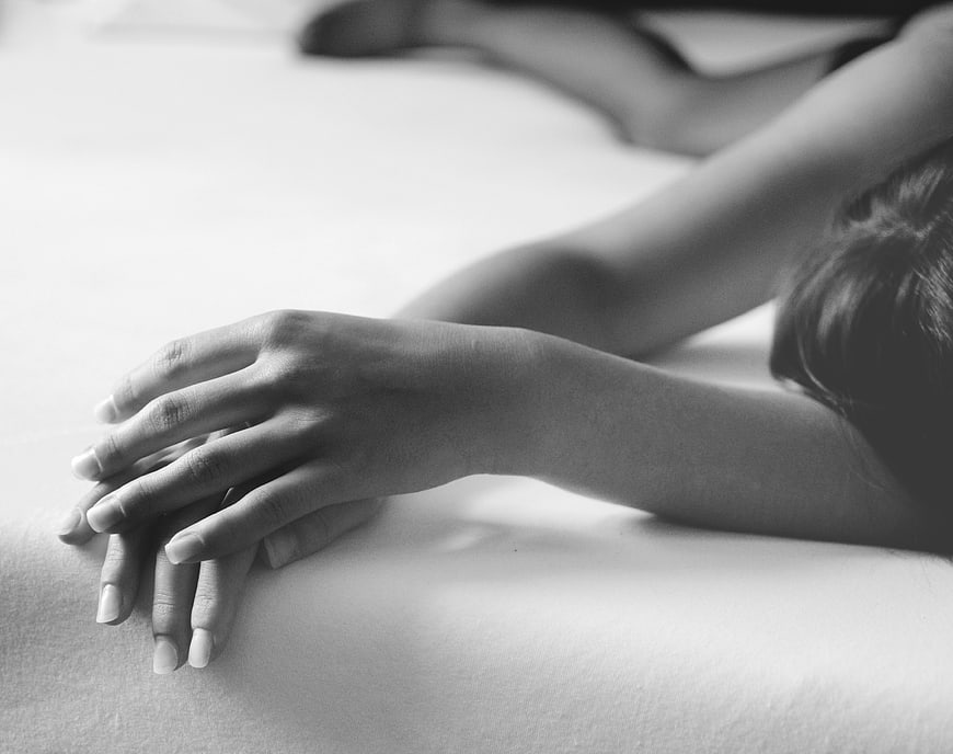 Black and white close-up of hands resting on a bed