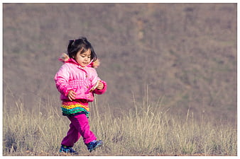 Young girl in pink jacket walking through dry grass field