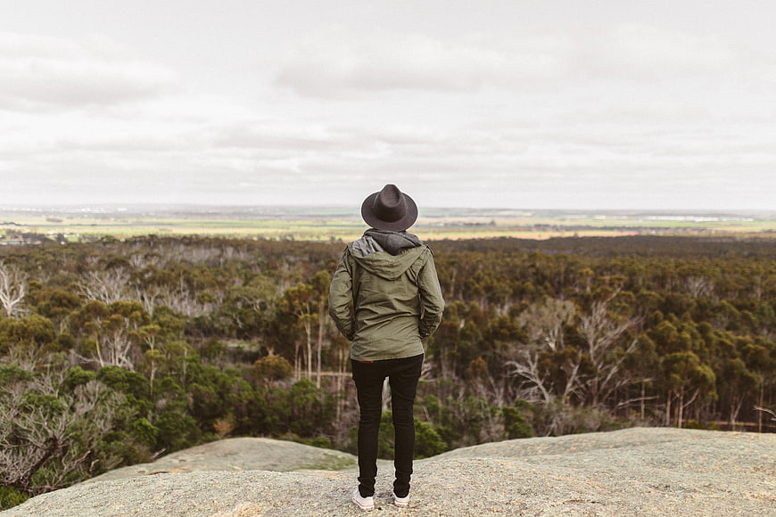 Woman in hat standing on rocky cliff overlooking forest valley