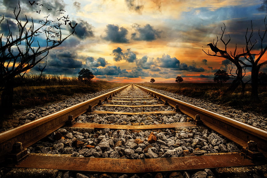 Dramatic Railroad Tracks Leading to Sunset Horizon with Silhouetted Trees