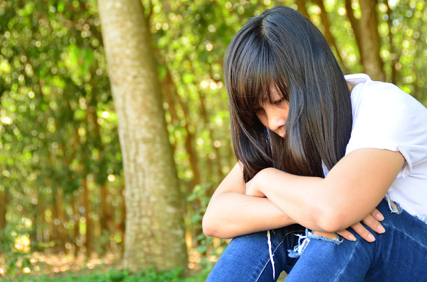 Sad Young Woman Sitting Alone in Forest
