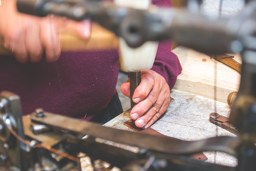 Close-up of hands using a chisel and hammer on leather