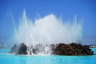 Dramatic water fountain spraying over rocks in turquoise pool