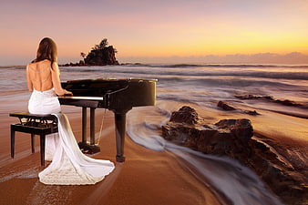 Woman in white dress playing grand piano on beach at sunset
