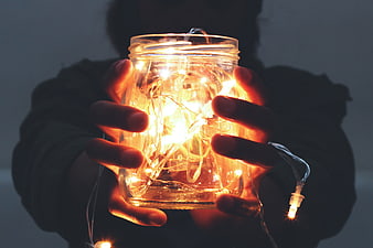 Hands holding a glass jar filled with glowing warm fairy lights