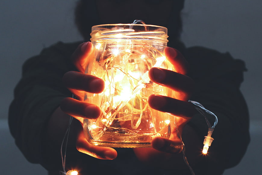 Hands holding a glass jar filled with glowing warm fairy lights
