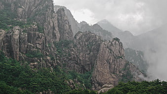 Misty granite mountain peaks with pine trees in foggy landscape