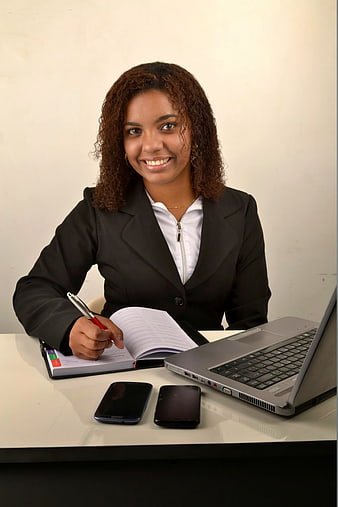 Smiling Businesswoman at Desk with Laptop and Notebook