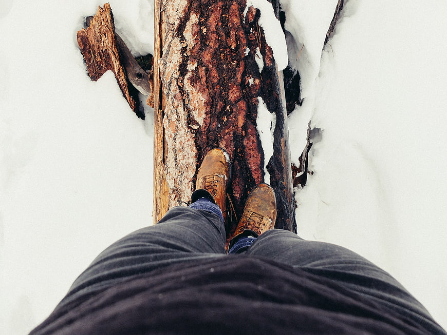 First-person view of boots walking on a log in snow