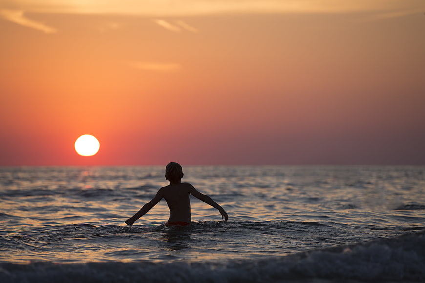 Silhouette of Boy Swimming in Ocean at Sunset