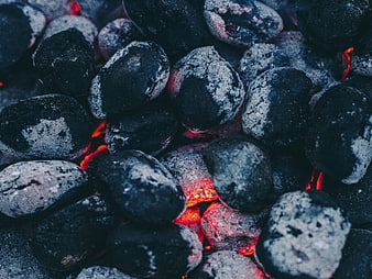 Close-up of glowing charcoal briquettes with ash and embers