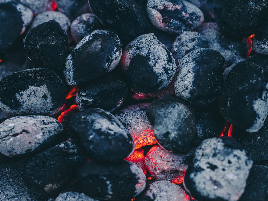 Close-up of glowing charcoal briquettes with ash and embers