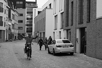 Cyclist with raised arms on cobblestone street with pedestrians and car