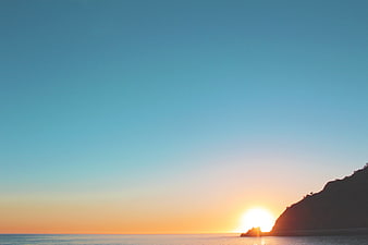 Serene Sunrise Over Ocean with Silhouetted Cliff