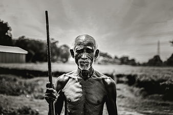 Portrait of an elderly Indian man holding a wooden staff in a rural field