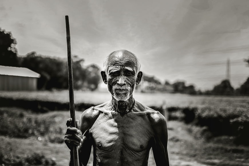 Portrait of an elderly Indian man holding a wooden staff in a rural field
