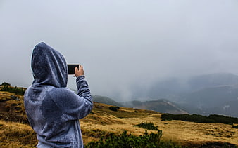 Person in Hoodie Taking Photo of Foggy Mountain Landscape
