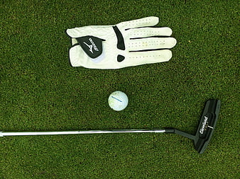 Golf putter, ball, and glove on green grass