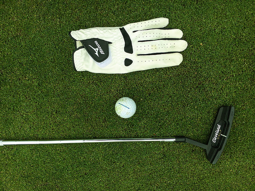 Golf putter, ball, and glove on green grass