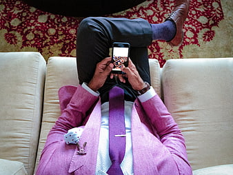 Man in pink suit using smartphone on beige sofa