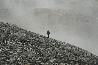 Lone hiker on rocky mountain ridge in thick fog