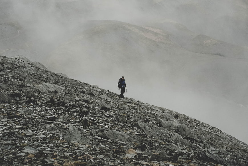 Lone hiker on rocky mountain ridge in thick fog