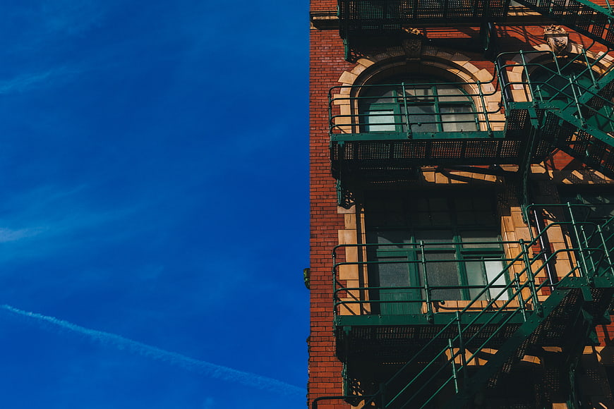 Red Brick Building with Green Fire Escape Against Blue Sky