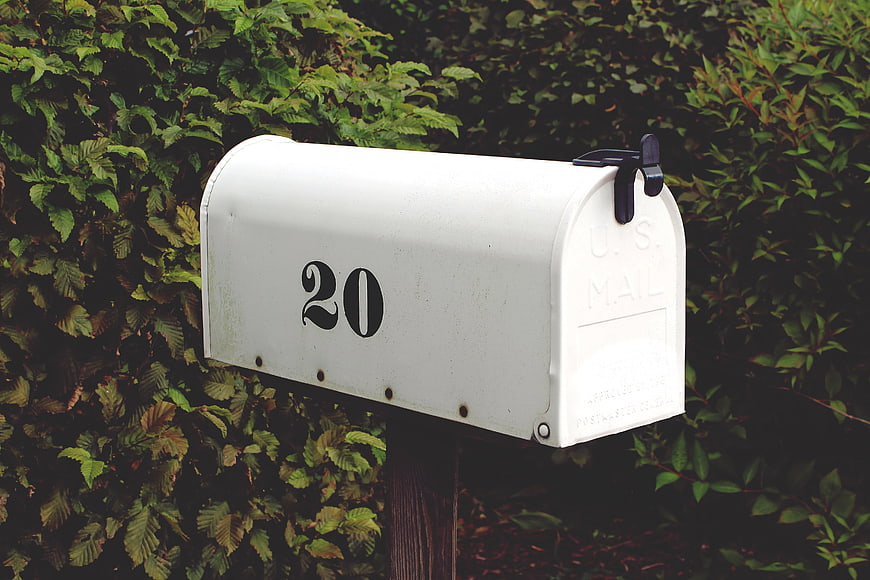 White U.S. Mailbox with Number 20 Against Green Bushes