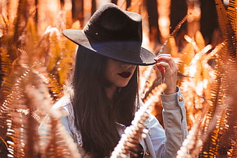 Woman in black hat holding brim in golden fern field