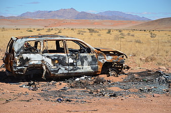 Burned Out Car Wreck in Arid Desert Landscape with Distant Mountains